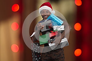 Man wearing santa claus hat and holding many christmas gifts boxes on red lights background