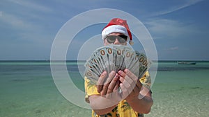 Man wearing Santa hat counting US dollars on tropical beach
