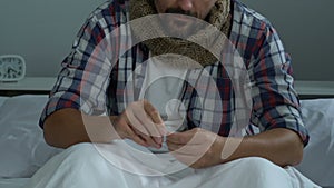 Man wearing scarf feeling sore throat, taking pills with water, cold treatment