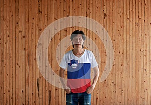 Man wearing Slovenia flag color shirt and standing with two hands in pant pockets on the wooden wall background