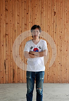 Man wearing South Korea flag color shirt and cross one`s arm on wooden wall background photo