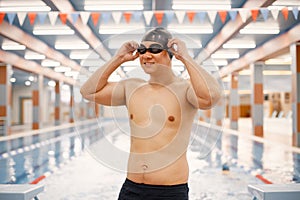 Asian man standing in indoors swimming pool and wearing a hat and goggles photo