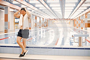 Asian man standing in indoors swimming pool with a towel on his shoulders photo