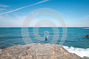 Man wearing sports clothes and carrying a backpack takes pictures of the Atlantic coastline near Porto Covo, Portugal. Capturing