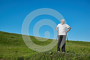 Man wearing sportsuit standing with tracking sticks on green hill.