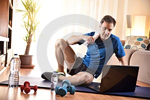 Man wearing sportswear on mat watching videos on a laptop