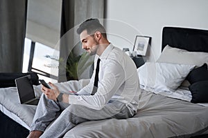 Man wearing suit sitting at the bed and looking at the smartphone screen