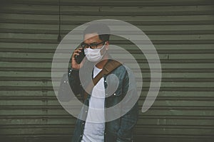 Man wearing surgical mask on street while using phone. Portrait of young man wearing a protective mask to prevent germs, toxic fum photo