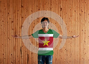 Man wearing Suriname flag color shirt and standing with arms wide open on the wooden wall background