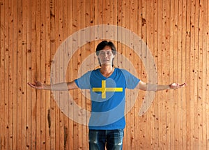 Man wearing Sweden flag color shirt and standing with arms wide open on the wooden wall background