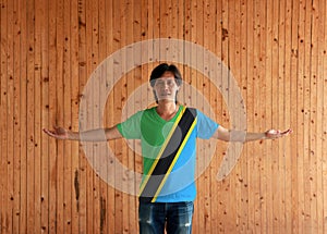 Man wearing Tanzania flag color shirt and standing with arms wide open on the wooden wall background