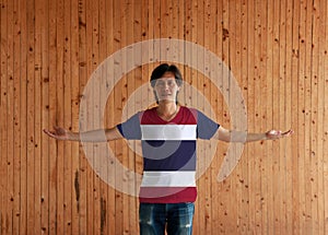 Man wearing Thailand flag color shirt and standing with arms wide open on the wooden wall background