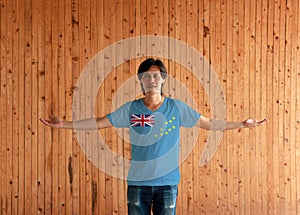 Man wearing Tuvalu flag color shirt and standing with arms wide open on the wooden wall background