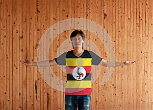 Man wearing Uganda flag color shirt and standing with arms wide open on the wooden wall background