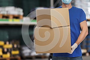 Man wearing uniform and medical mask with cardboard boxes in store. Wholesale market