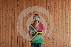 Man wearing Vanuatu flag color of shirt and standing with crossed behind the back hands on the wooden wall background