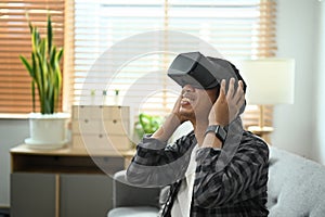 Man wearing virtual reality glasses for watching video or play video game on sofa at home.