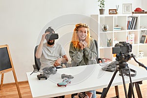 Man wearing vr glasses, while woman smiling to camera. Young male and female technology blogger recording video blog or