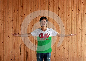 Man wearing Wales flag color shirt and standing with arms wide open on the wooden wall background