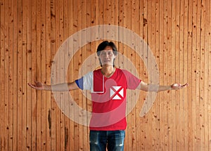 Man wearing Wallis and Futuna flag color shirt and standing with arms wide open on the wooden wall background
