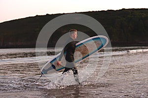 Man Wearing Wetsuit Carrying Surfboard As He Walks Out Of Sea