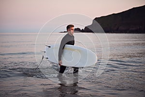 Man Wearing Wetsuit Carrying Surfboard As He Walks Out Of Sea