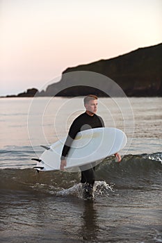 Man Wearing Wetsuit Carrying Surfboard As He Walks Out Of Sea