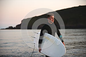 Man Wearing Wetsuit Carrying Surfboard As He Walks Out Of Sea