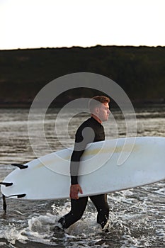 Man Wearing Wetsuit Carrying Surfboard As He Walks Out Of Sea