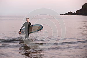 Man Wearing Wetsuit Carrying Surfboard As He Walks Out Of Sea