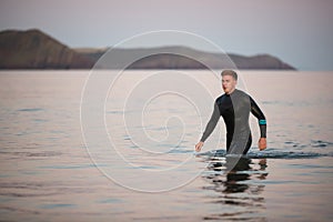 Man Wearing Wetsuit Wading Through Shallow Sea By Shore