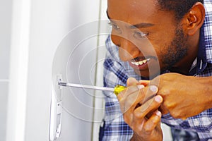 Man wearing white and blue shirt working on electrical wall socket using screwdriver, electrician concept