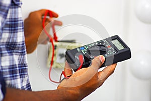 Man wearing white and blue shirt working on electrical wall socket wires using multimeter, electrician concept