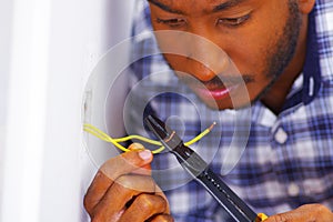 Man wearing white and blue shirt working on electrical wall socket wires using screwdriver, electrician concept photo