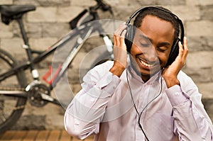 Man wearing white red business shirt sitting down with headphones on, enjoying music while smiling happily, bicycle