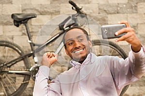 Man wearing white red business shirt sitting down, holding up mobile phone taking selfie photo, smiling and posing