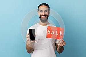 Man wearing white T-shirt holding sale card and smartphone, being satisfied with online sell-out.