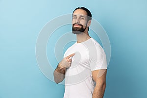 Man wearing white T-shirt pointing at himself, feeling proud and self-important, having big ego.