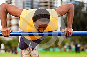 Man wearing yellow shirt and blue shorts doing static strength excercises hanging from pole, outdoors training facility