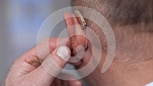 Man wears a hearing aid. Senior man with symptom of hearing loss. Mature tensed man with fingers near ear. Man with