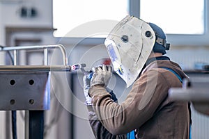 A man in a welding helmet is using gas to weld metal in a factory