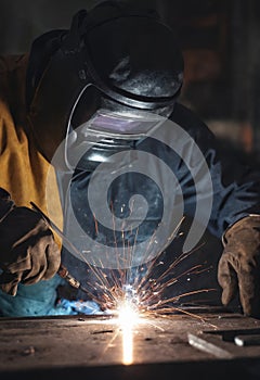 A man in a welding mask fusing metal with Electric blue light in darkness