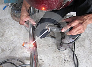 The man welding a stainless steel pipe using agronomic welding to protect his eyes with a mask in workshop