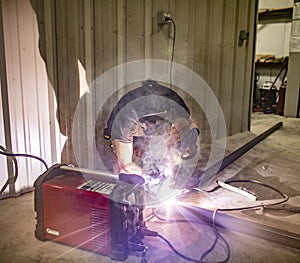A man welds two pieces of metal together with an arc welder in a shop