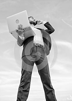 Man well groomed businessman holds laptop while speak phone blue sky background. Guy formal suit modern technology