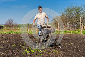 Man in wellingtons with cultivator ploughing ground in sunny day. Farmer plowing kitchen-garden in suburb. Land cultivation, soil