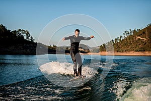 man in wetsuit energetically balancing on river water on a foil wakeboard on beautiful landscape background.