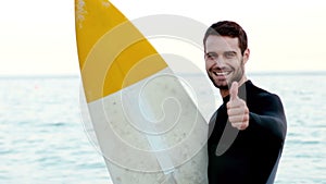 Man in wetsuit with a surfboard gesturing thumbs up