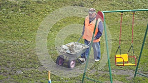 Man with a wheelbarrow with garbage is walking on the grass and the path