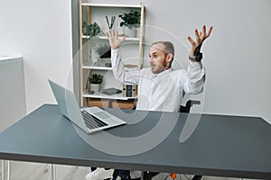 A man in a wheelchair businessman with tattoos in the office behind a laptop, anger and annoyance, hands up, the concept